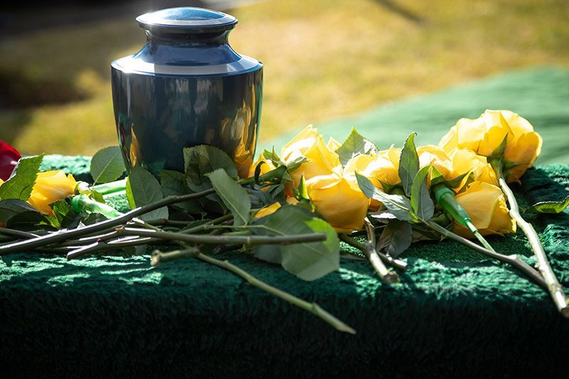 A urn surrounded by yellow roses and leaves on a table.
