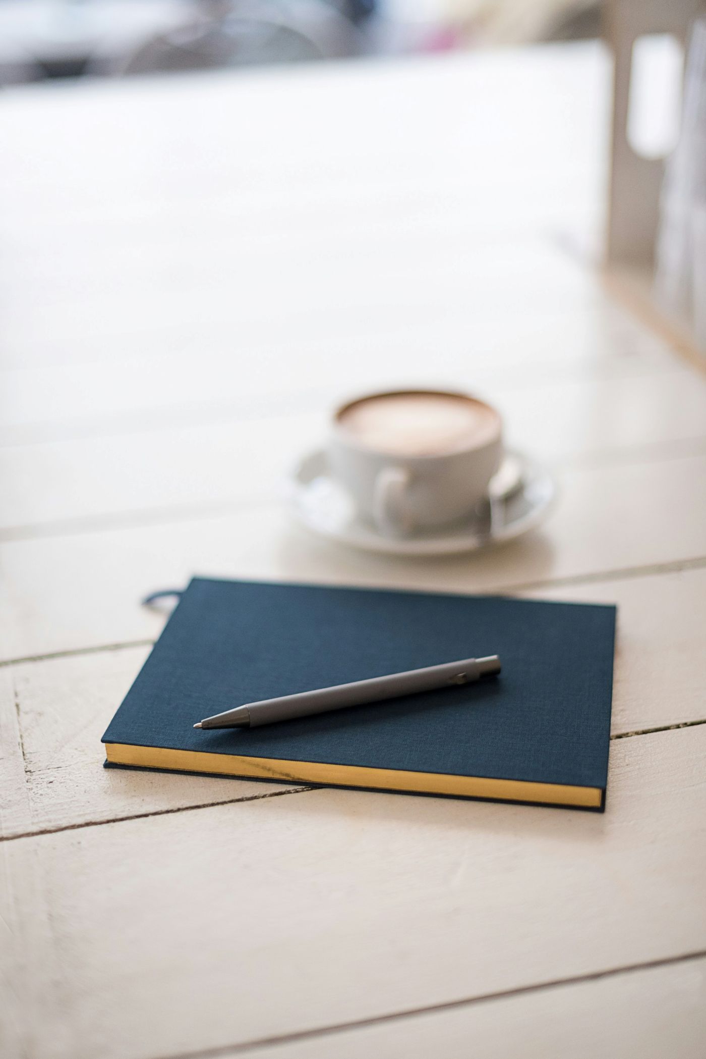 A notebook and pen are on a table next to a cup of coffee.