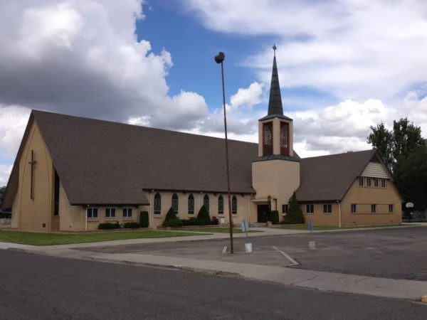 A church with a steeple in the middle of a parking lot