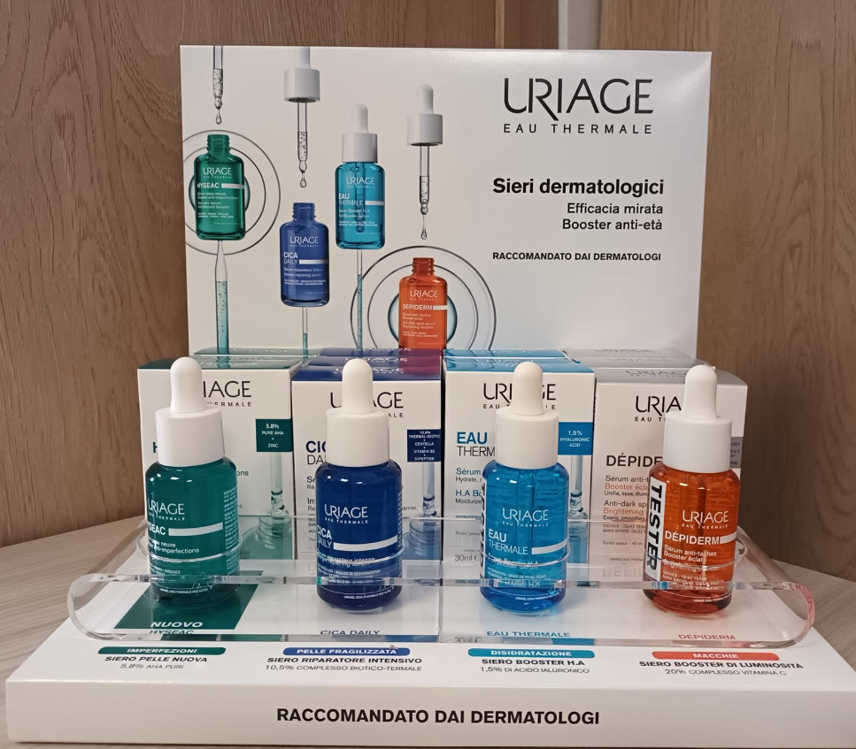Espositore per prodotti per la cura della pelle URIAGE con quattro flaconi di siero colorati e un cartello con raccomandazione dermatologica.