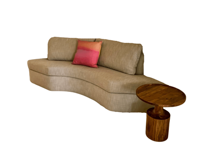Beige curved sofa with a pink/orange pillow, next to a round wooden side table.
