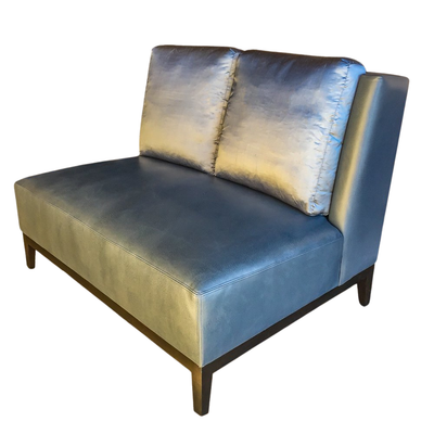 Gray leather loveseat with a single pillow and dark wood legs against a white background.