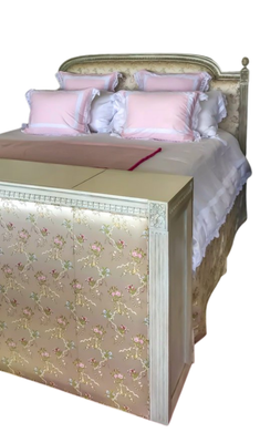 Bed with pink pillows and floral bench at the foot of it.