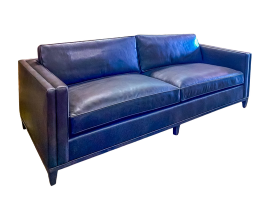 Blue leather sofa with two cushions, dark frame, white stitched seams, and short legs.