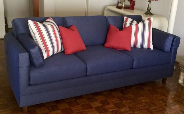 Navy blue couch with red and white striped and solid red pillows in a living room.