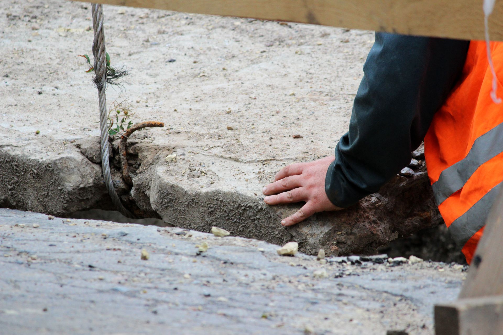 Worker in orange safety vest inspecting a cracked concrete curb and drainage ditch