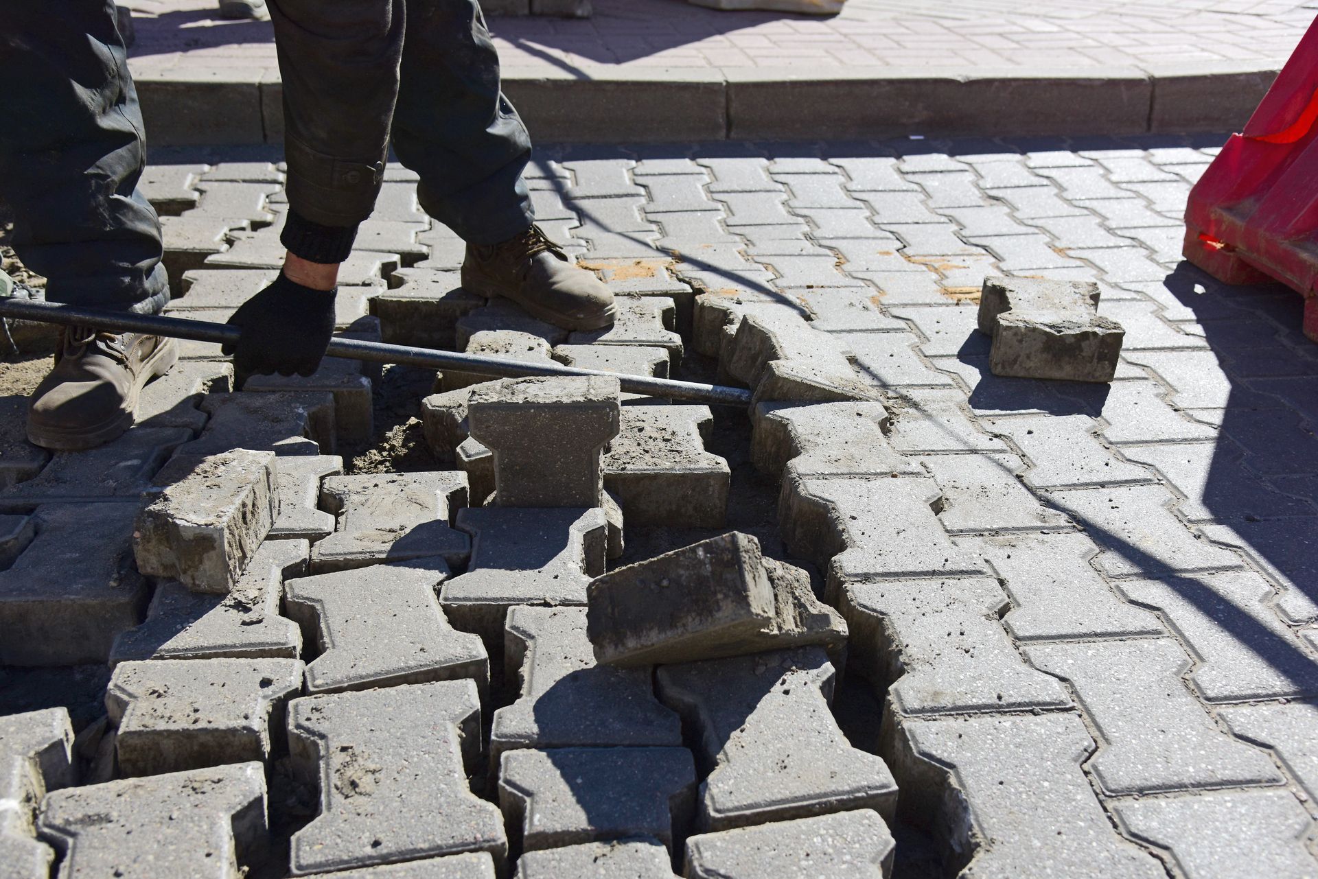 Damaged pavement with broken concrete blocks and two people’s legs standing nearby