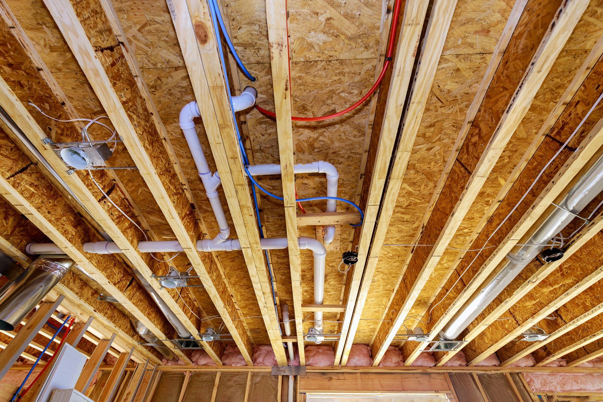 Exposed basement ceiling framing with pipes, ducts, and electrical wiring during construction