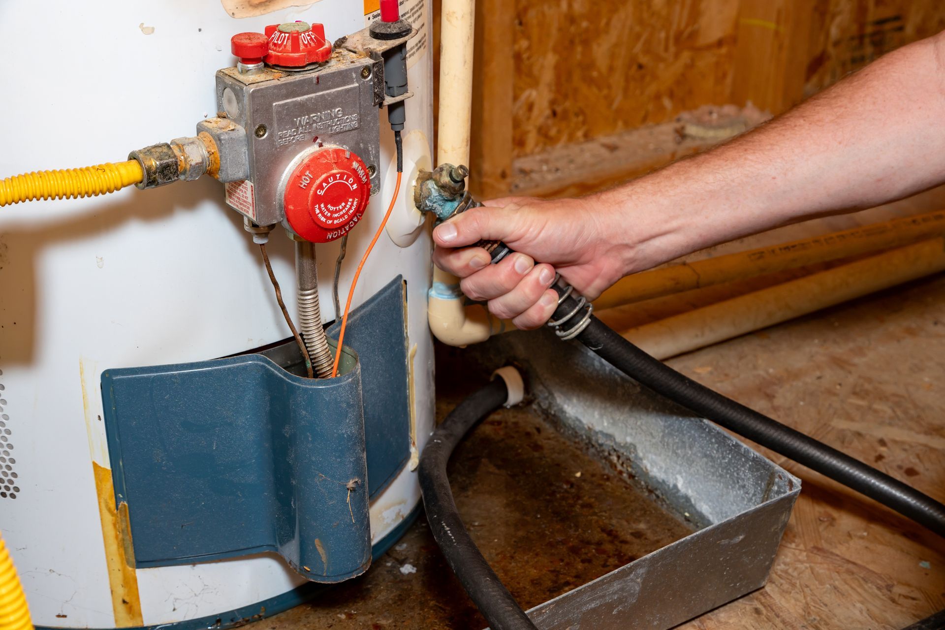 Plumber draining a tank water heater with a hose into a drain pan. Plumber draining a tank water heater with a hose into a drain pan.