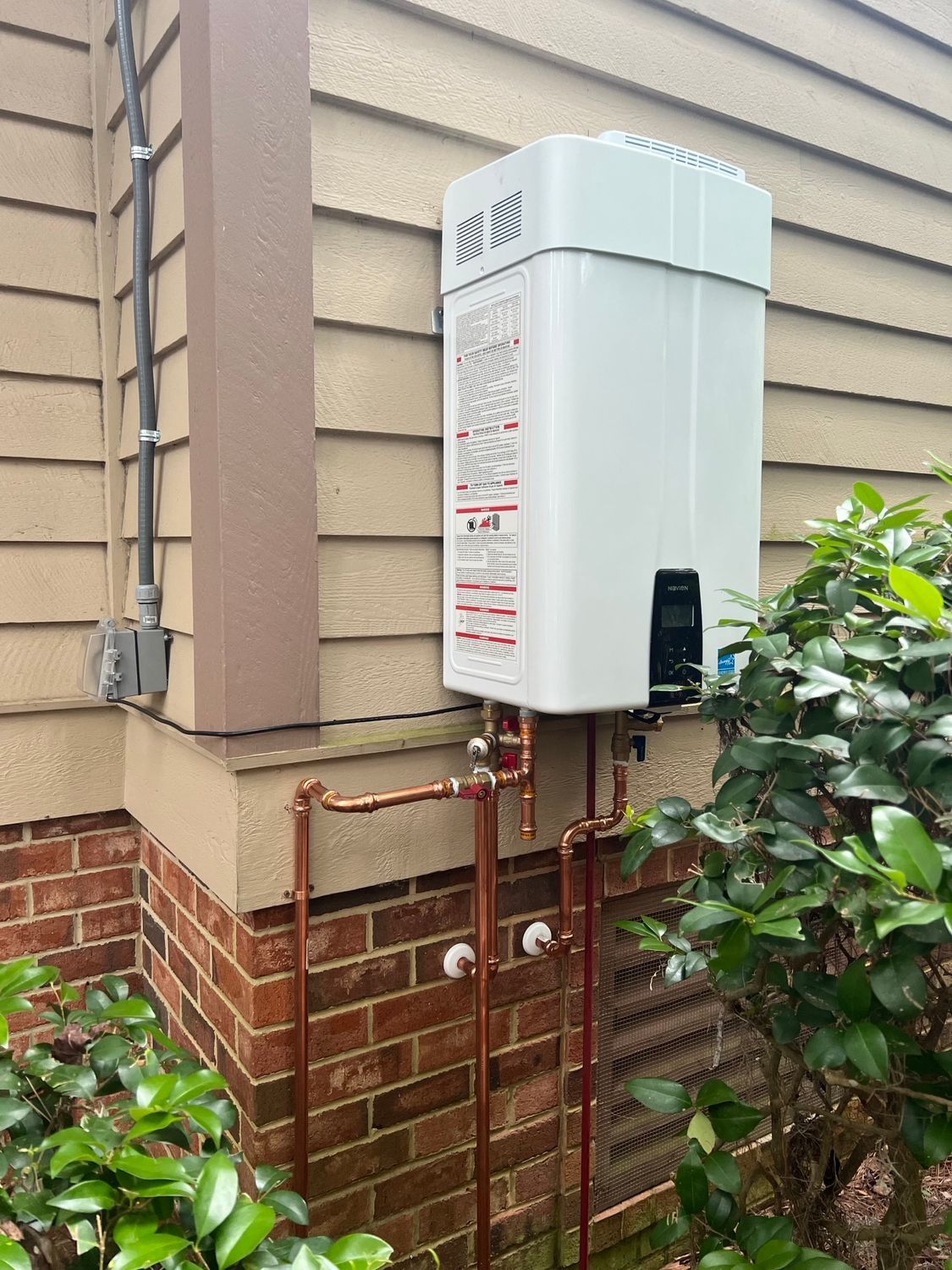 Wall-mounted tankless water heater with copper pipes on the side of a house