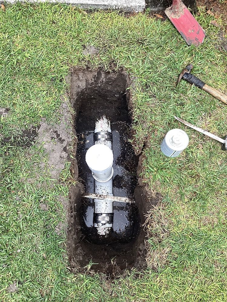Open water meter pit in grass with exposed pipe, tools, and a white cap nearby.
