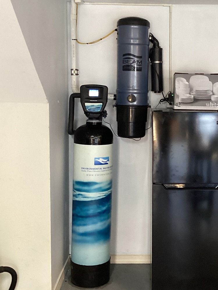 Two water softener/filter tanks with a control head beside a refrigerator in a small utility nook