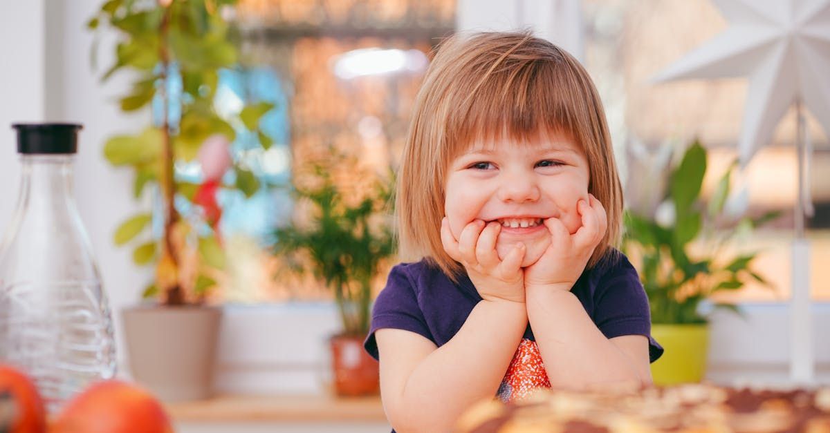 A little girl is sitting at a table with her hands on her chin.