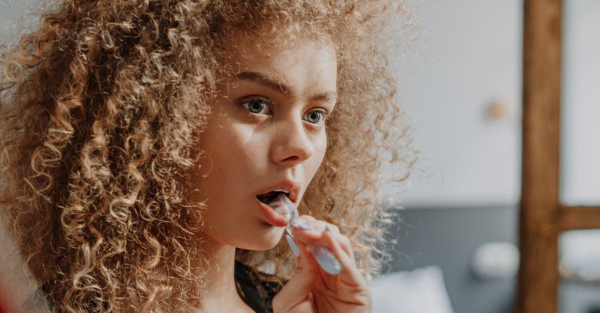 A woman with curly hair is brushing her teeth in front of a mirror.