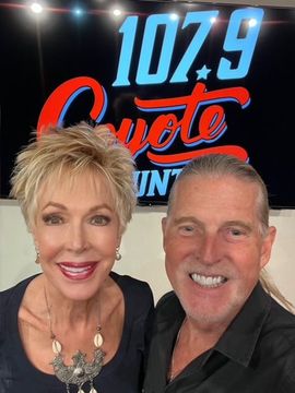 A man and a woman are posing in front of a 107.9 coyote sign