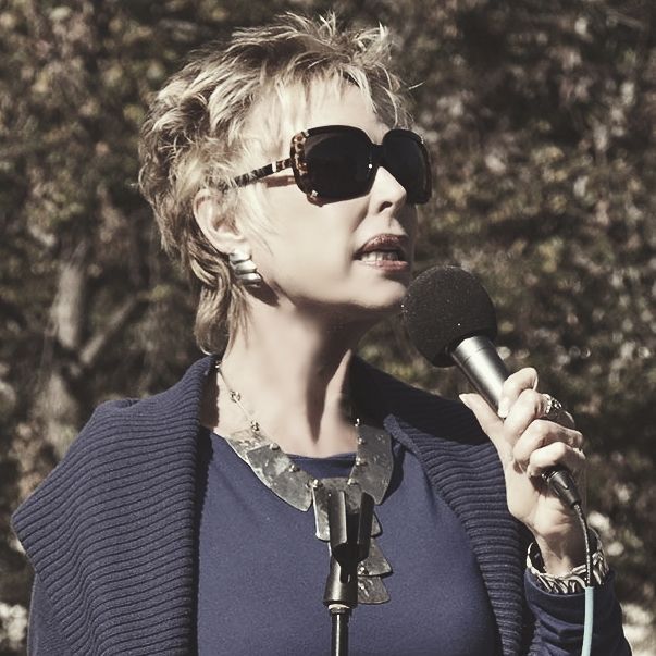 A woman wearing sunglasses is singing into a microphone