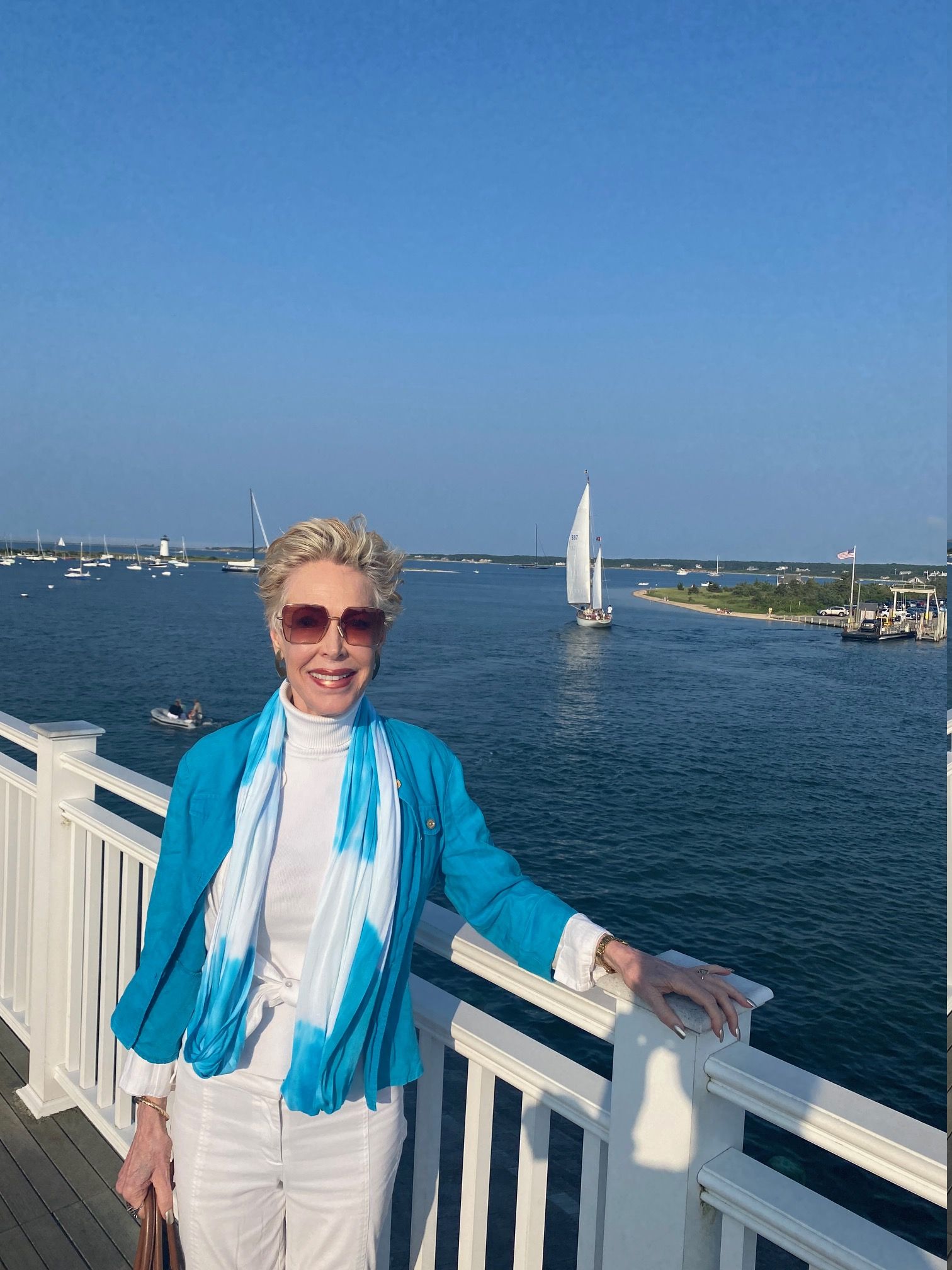 A woman in a blue jacket and white pants is leaning on a railing overlooking a body of water.