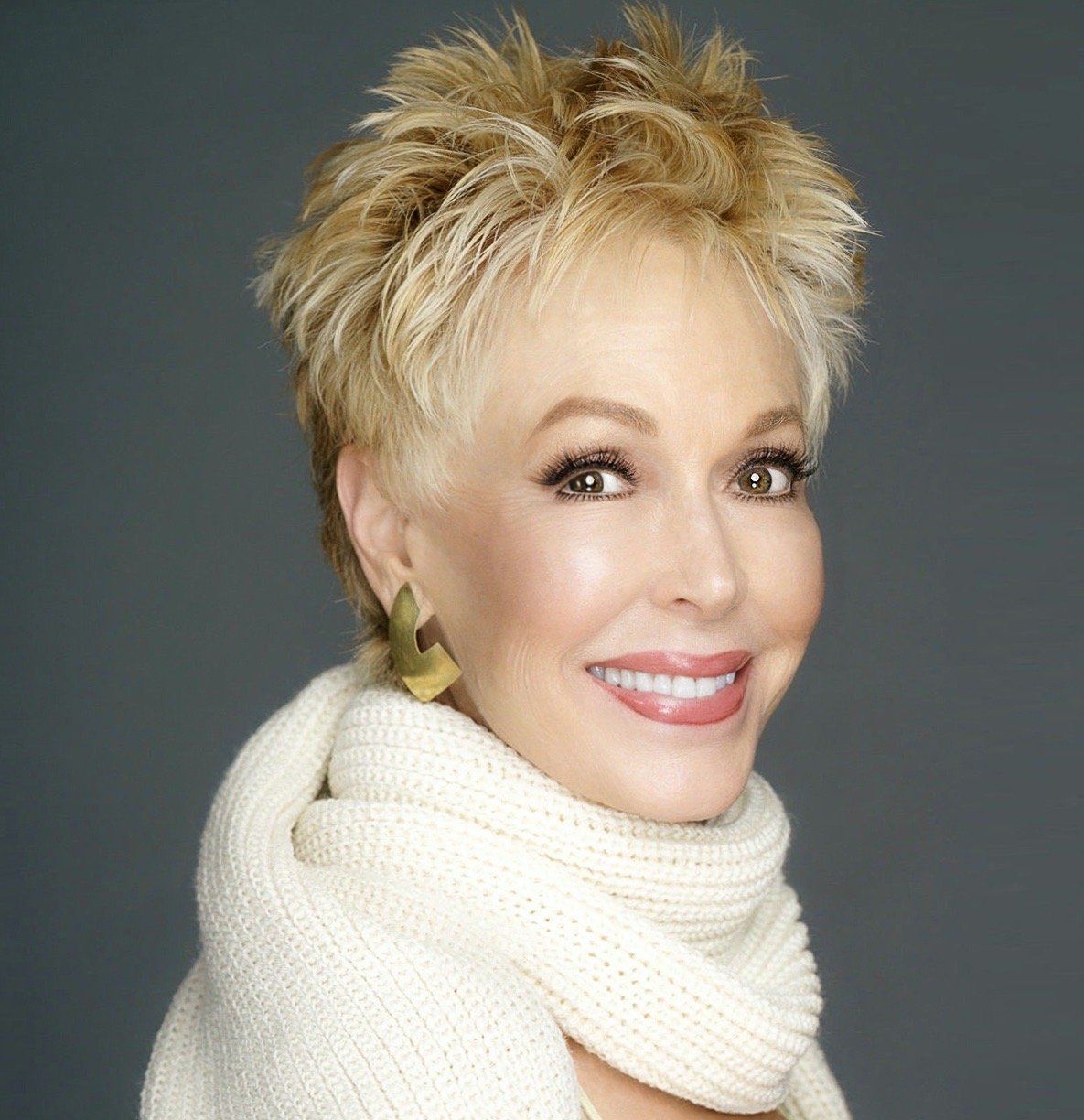 A woman wearing a white scarf and earrings smiles for the camera.