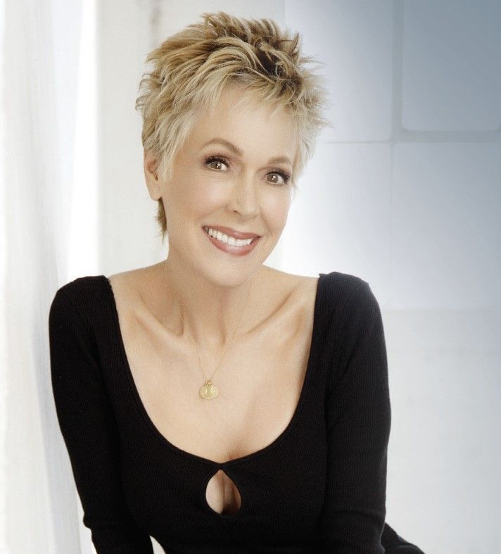 A woman wearing a black top and a necklace smiles for the camera