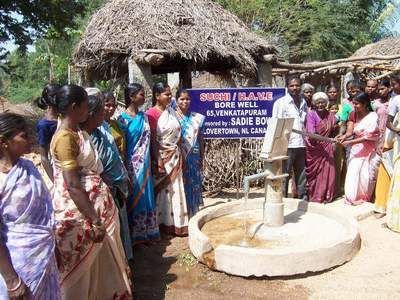 People gather around a new well. Women in saris and others look on in a rural setting.