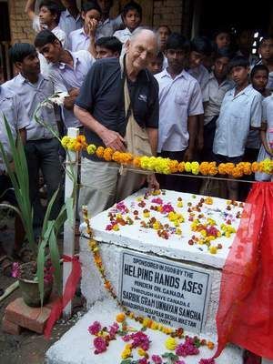 Man with students at a stone monument decorated with flowers.