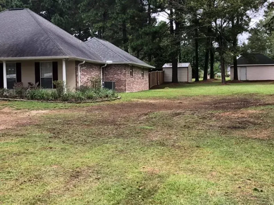 A house is sitting on top of a lush green field surrounded by trees.