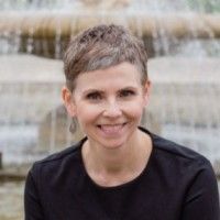 A woman is sitting in front of a fountain and smiling.