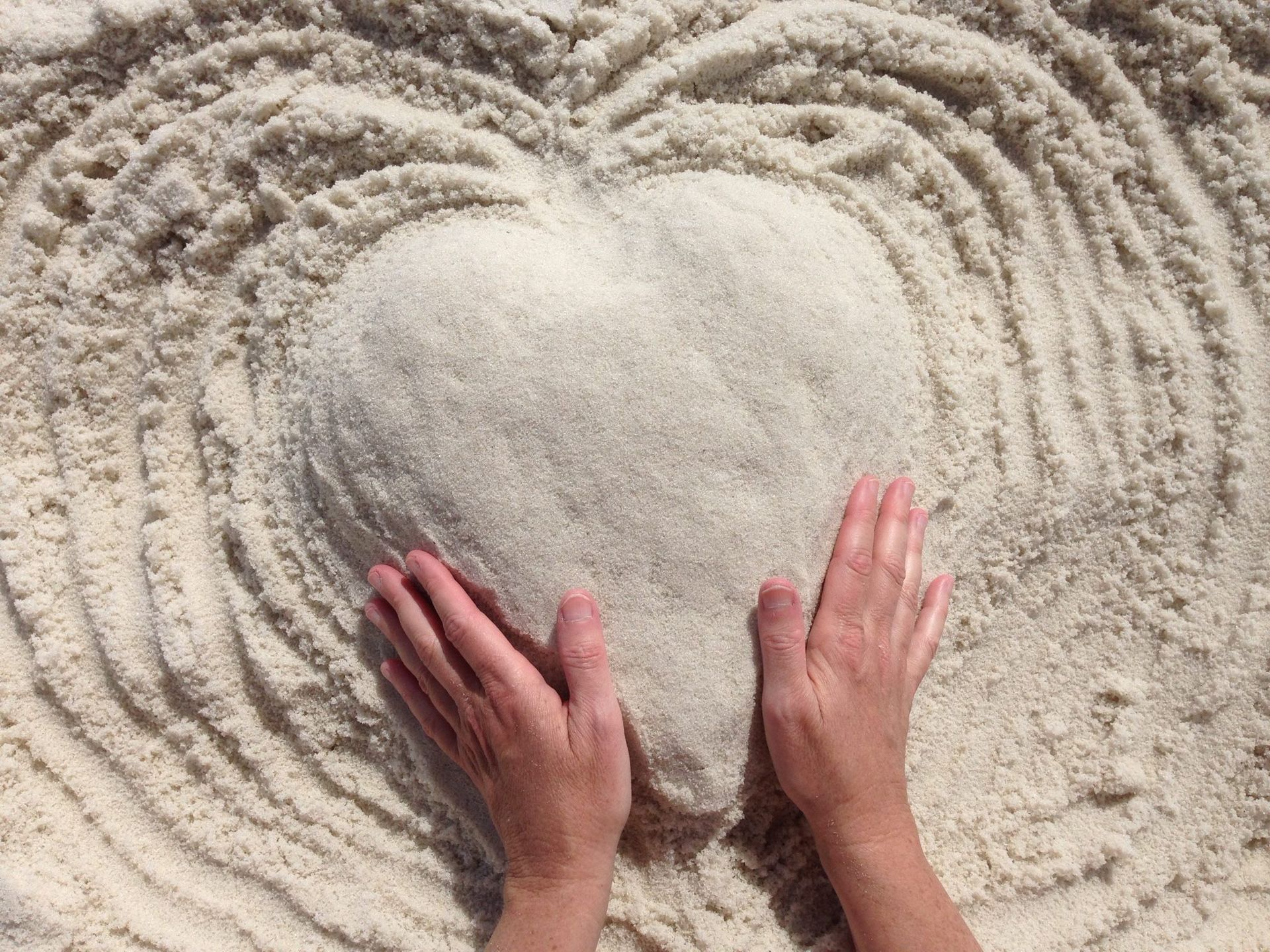 two hands mold sand into a heart shape