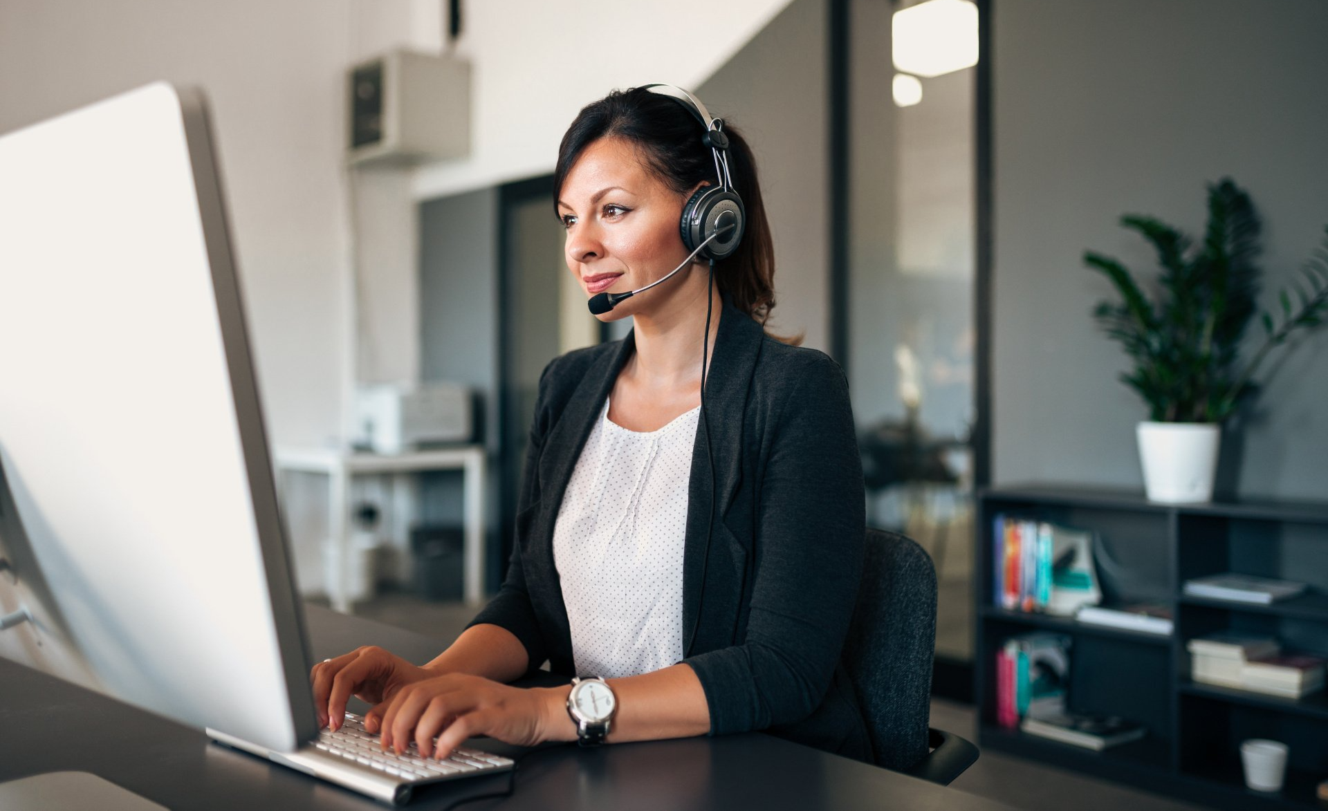 A woman wearing a headset is sitting at a desk in front of a computer.