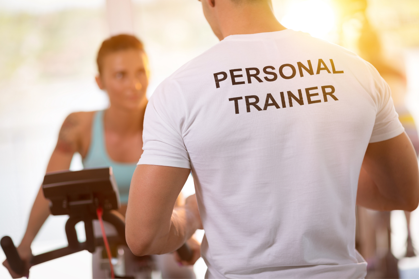 a man wearing a personal trainer shirt is helping a woman on an exercise bike