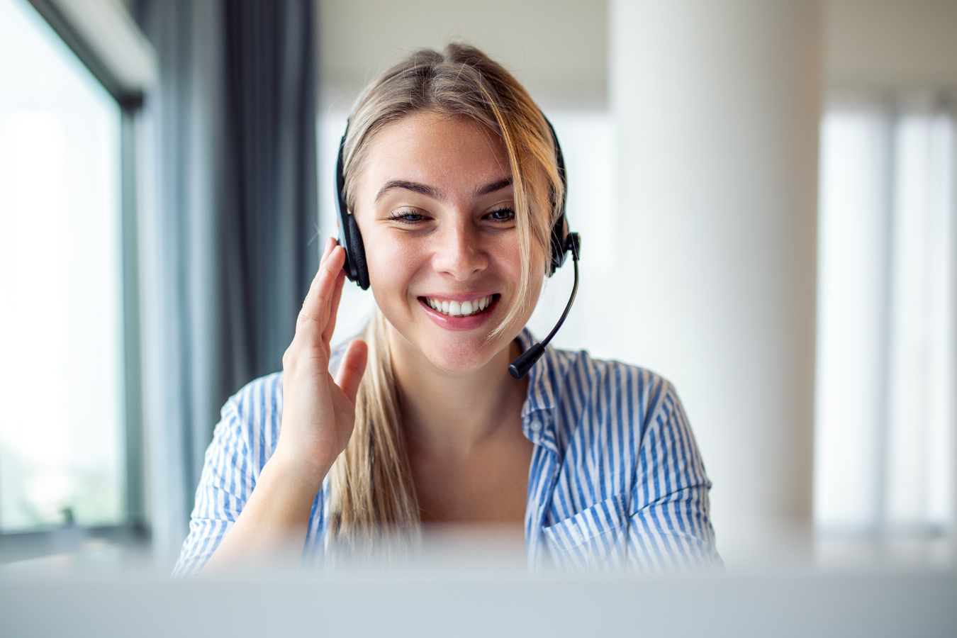 A woman wearing a headset is sitting in front of a laptop computer.