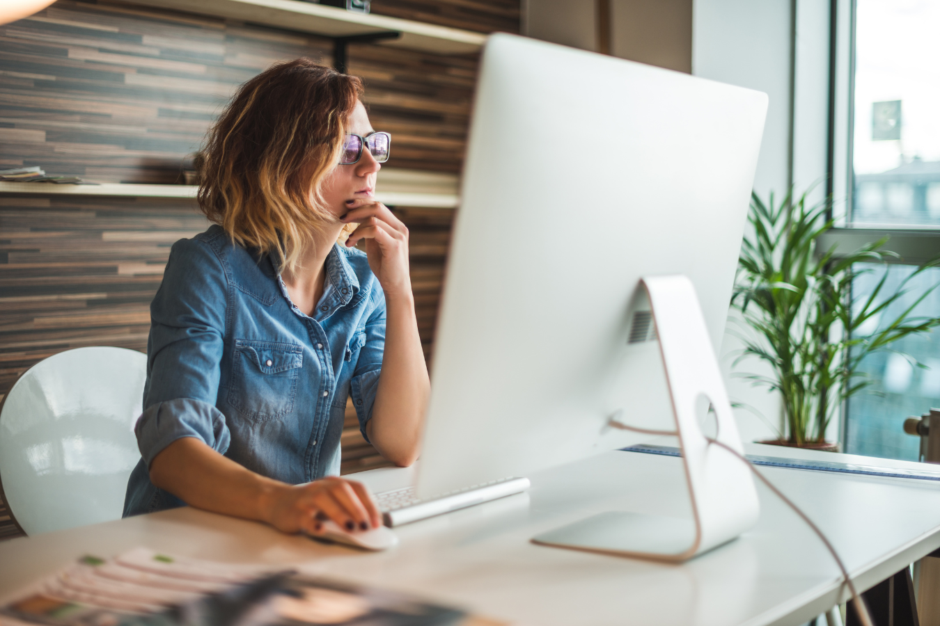 A woman is sitting at a desk in front of a computer monitor.
