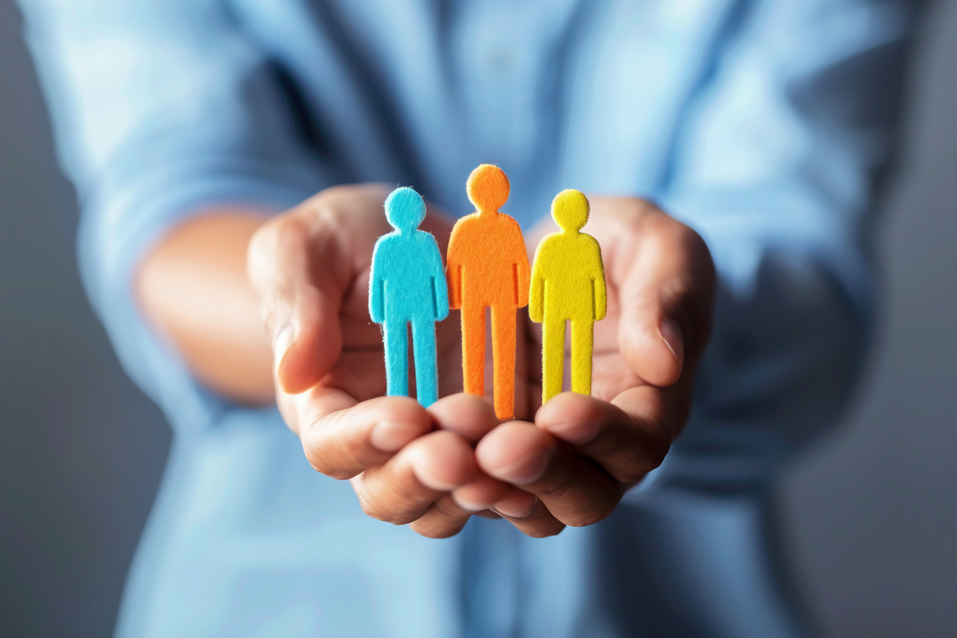 A virtual assistant's hands  support a representation of clients in the form of paper dolls.