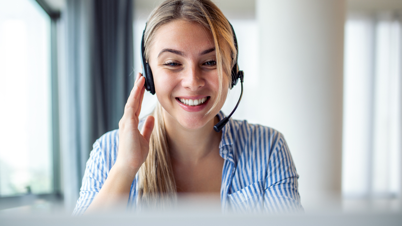 A woman wearing a headset is smiling while talking on a video call.