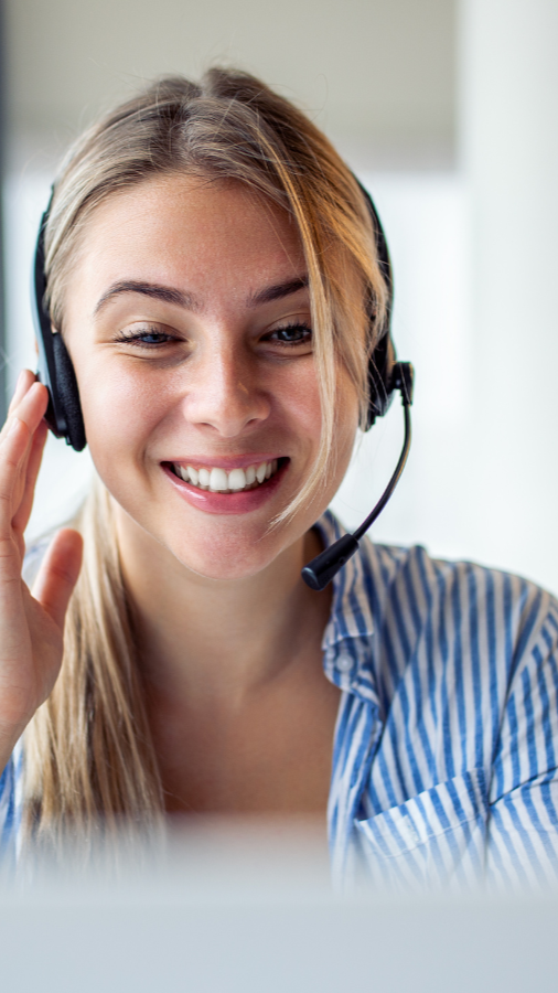 Woman with blonde hair wearing headset, smiling, working on laptop.