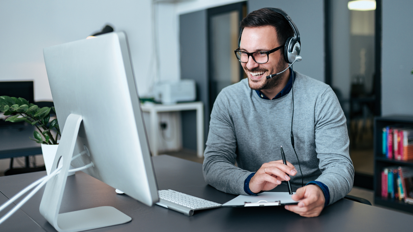 A man wearing headphones is sitting at a desk in front of a computer.