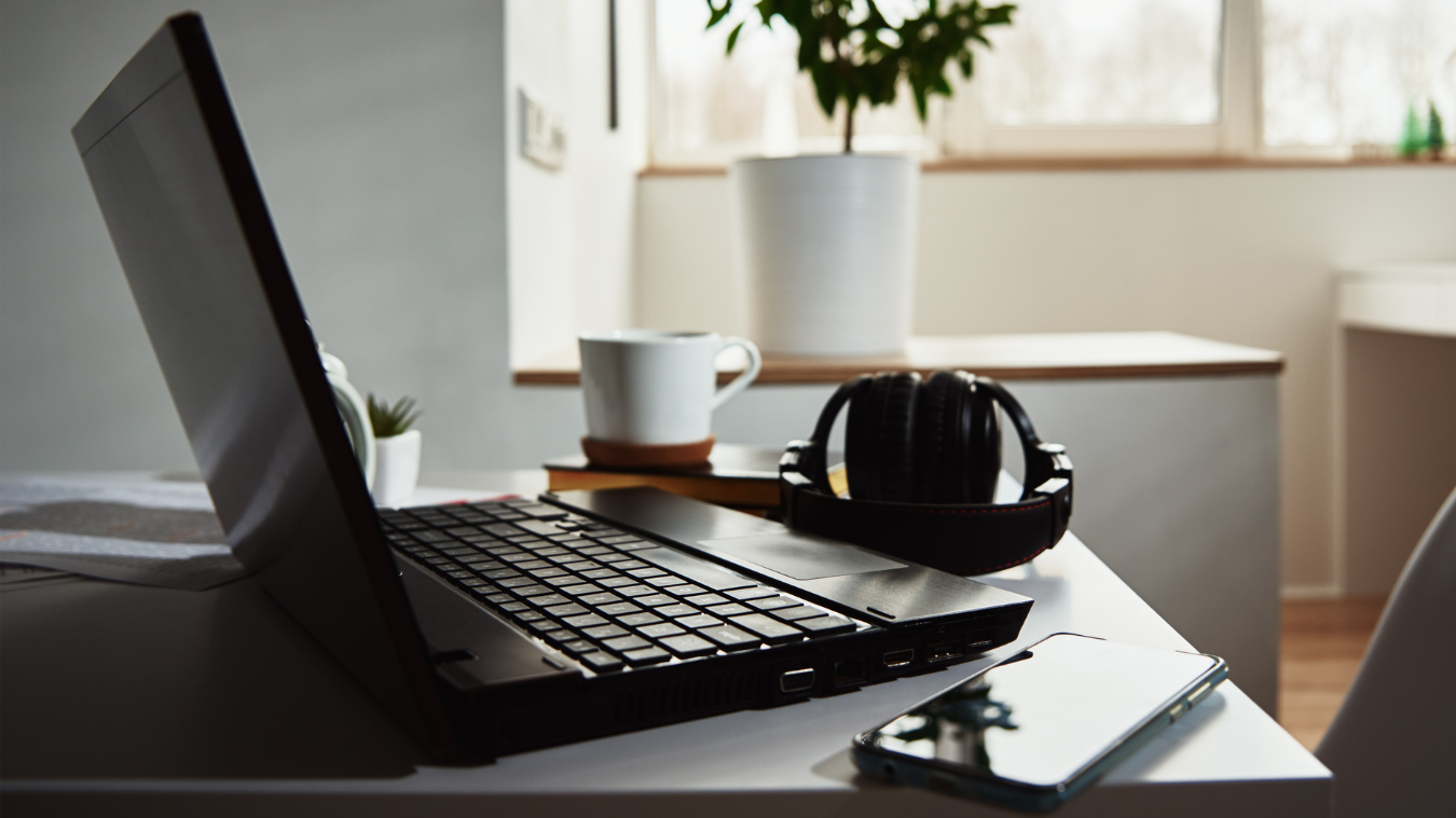 A laptop is sitting on a desk next to a cup of coffee and headphones.