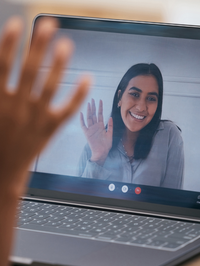 a person is waving at a woman on a laptop screen