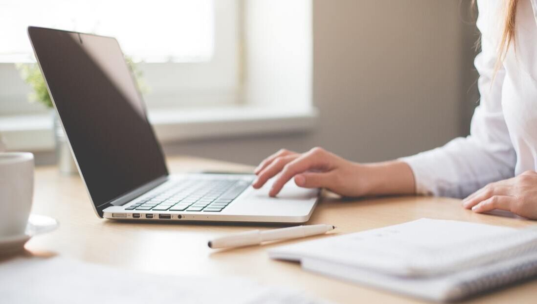 A woman is typing on a laptop computer while sitting at a desk.