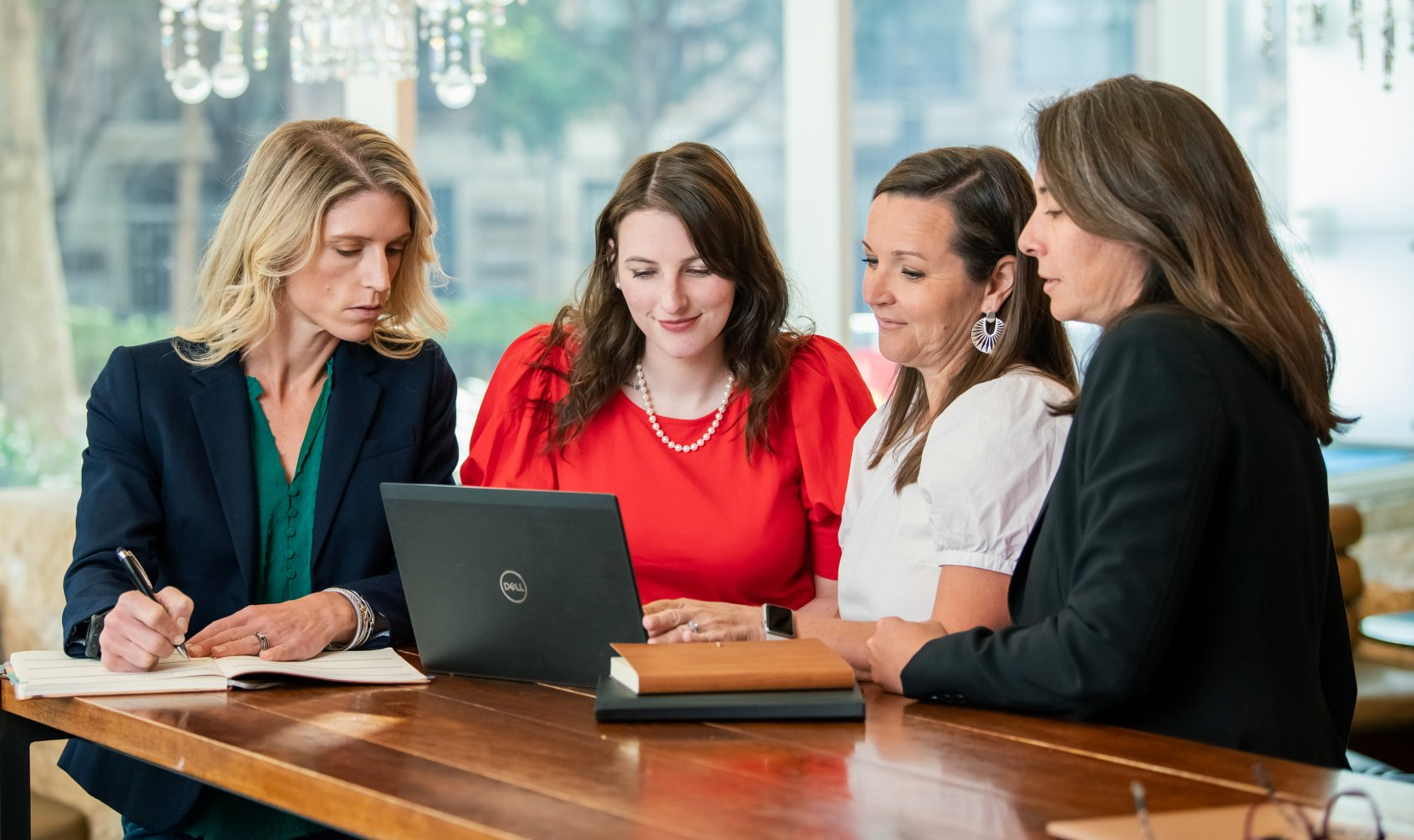 A group of women are sitting at a table looking at a laptop computer.