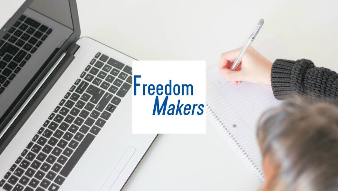 A person is writing in a notebook in front of a laptop with freedom makers written on it