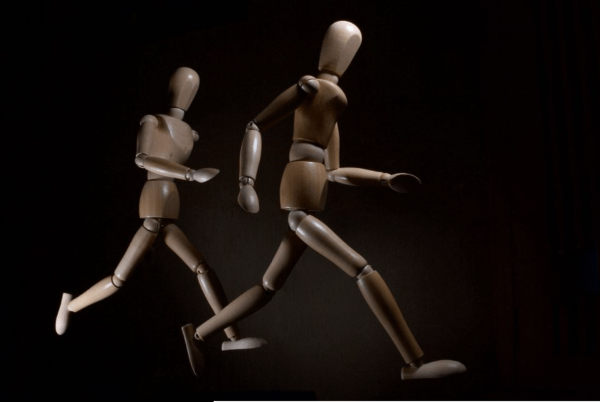 Two wooden mannequins are running in a dark room