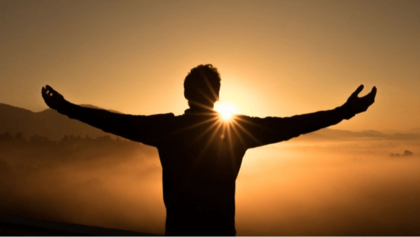 A man is standing with his arms outstretched in front of the sun.
