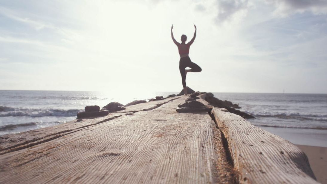 A person is doing yoga on a wooden pier near the ocean.