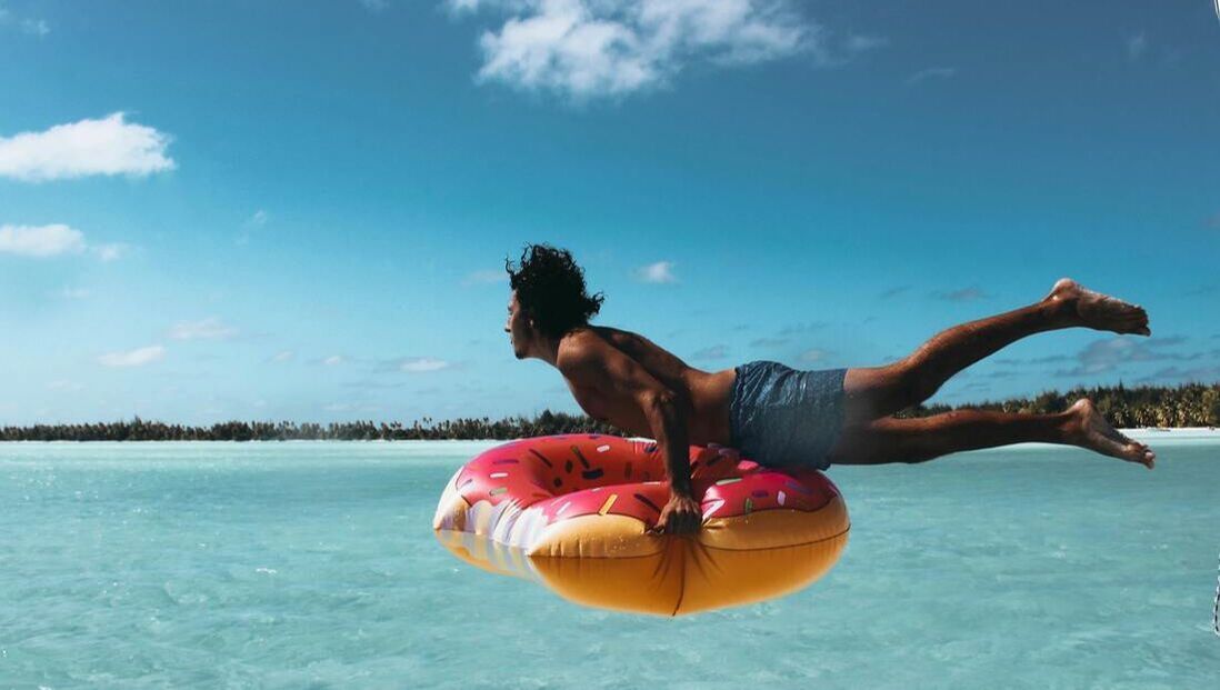 A man is floating on an inflatable donut in the ocean.