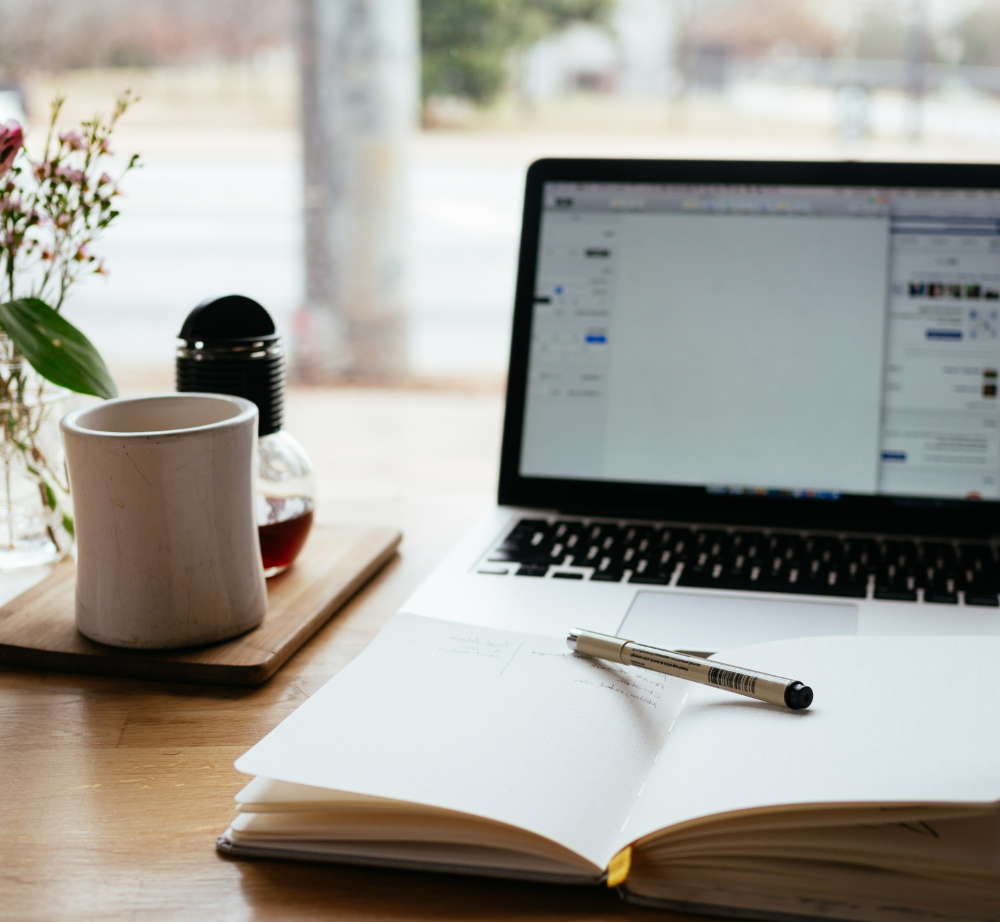 A laptop is open on a desk next to a notebook and pen