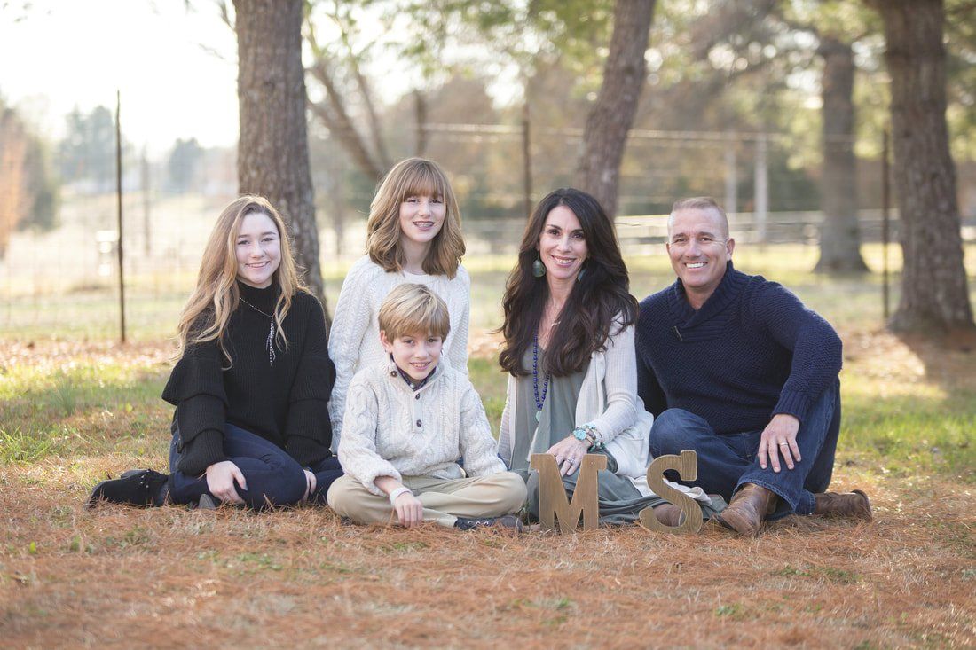 A family is posing for a picture while sitting on the ground in a park.
