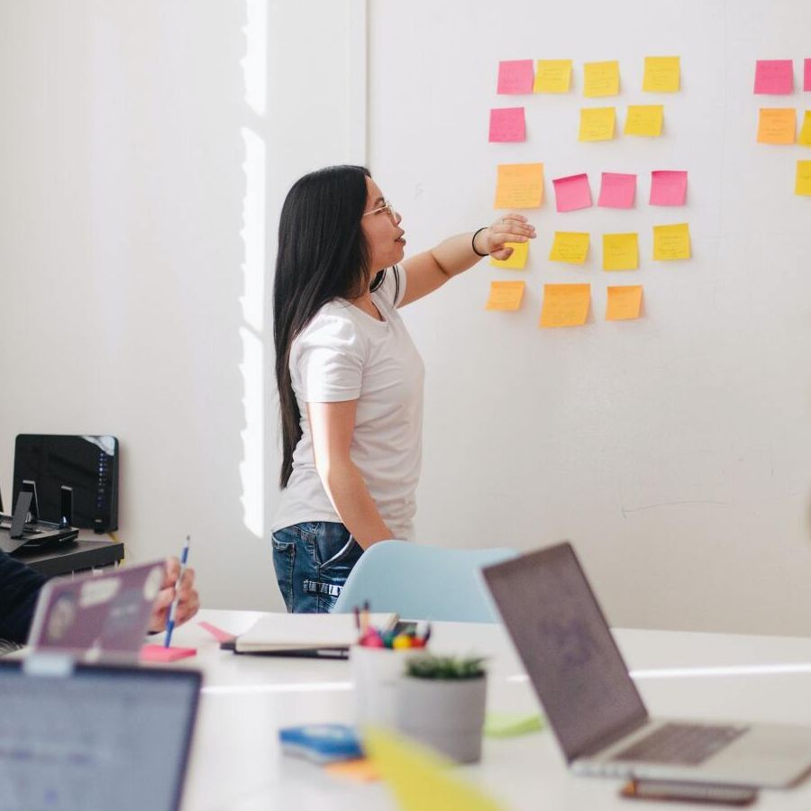 A woman is standing in front of a white board with sticky notes on it.