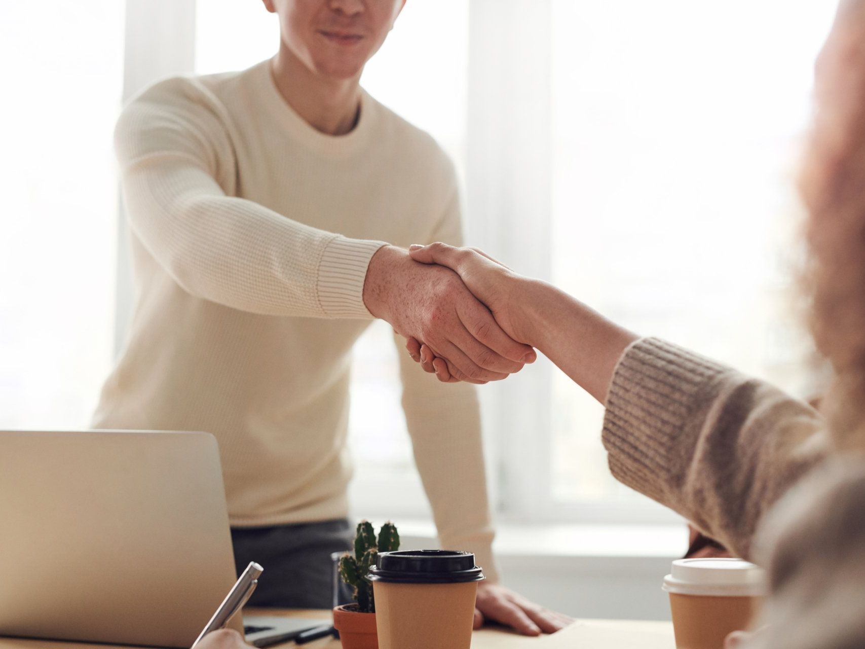 A man and a woman shake hands over a desk.