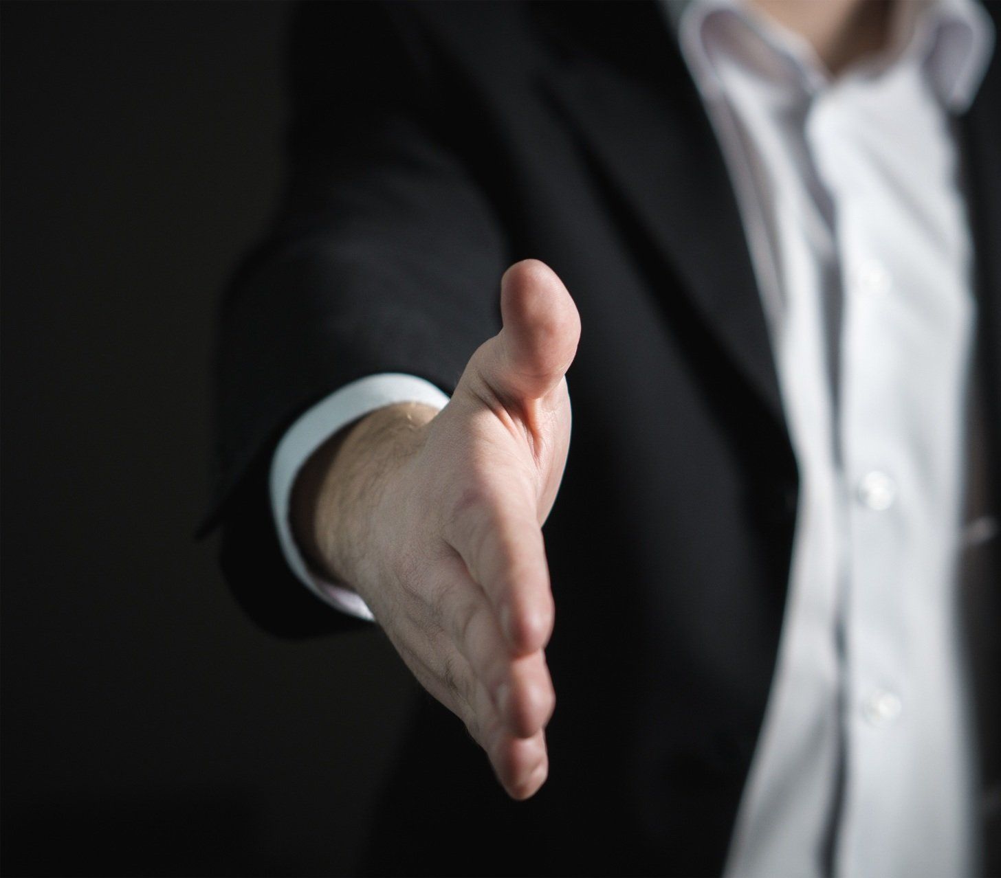 A man in a suit is reaching out his hand to shake someone 's hand.